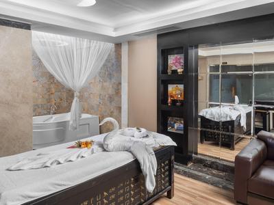 Heller Wellnessraum mit Badewanne, Massagebett, Spiegelwand und Ledersessel.