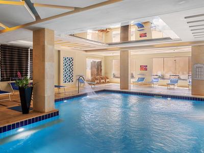 Innenpool mit blauem Wasser, Holzverkleidung und Loungemöbeln in einem Hotel.