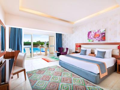 Hell eingerichtetes Hotelzimmer mit großem Bett, Balkon und Blick auf den Pool.
