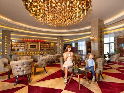 Luxuriöse Hotellobby mit gemütlichen Sesseln, Teppichboden und großem Kronleuchter an der Decke.