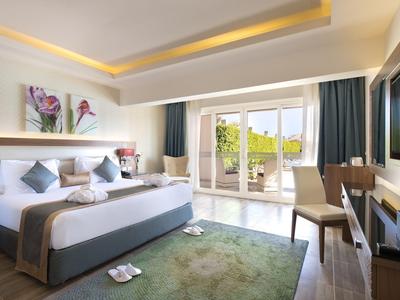 Heller Hotelraum mit großem Bett, Teppich, Stühlen und Balkon mit Ausblick auf die Natur.