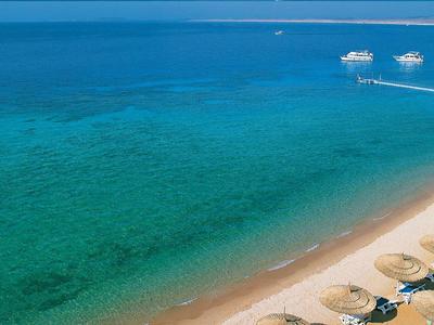 Ein türkiser Ozean mit Booten und einem Sandstrand mit Liegestühlen und Sonnenschirmen.