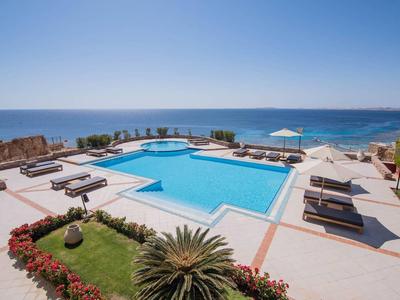 Pool mit Liegen und Blick aufs Meer in einem Hotelresort bei klarem Himmel.