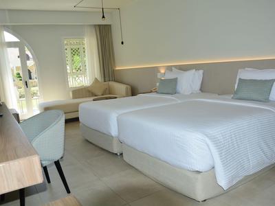 Modern eingerichtetes Hotelzimmer mit zwei Einzelbetten, Schreibtisch und Sofa in neutralen Farben.