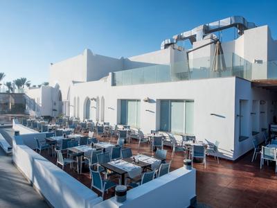 Moderne Außenterrasse eines Hotels mit weißen Tischen und Stühlen unter klarem Himmel.