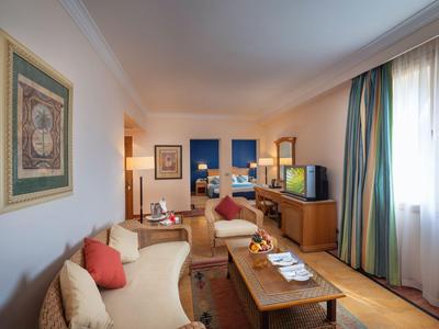 Helles Hotelzimmer mit zwei Sofas, Holztisch und Fenster mit Vorhängen.