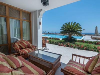 Gemütliche Terrasse mit gepolsterten Stühlen, Tisch und Blick auf Pool und Meer.