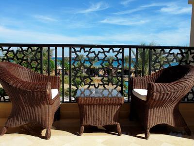 Balkon mit zwei geflochtenen Stühlen und Tisch mit Meerblick und blauem Himmel.