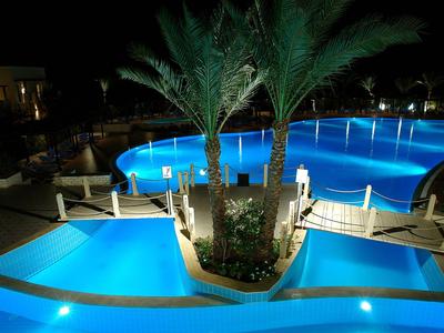Beleuchteter Hotelpool bei Nacht mit Palmen und ruhigem Wasser.