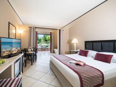 Modernes Hotelzimmer mit Doppelbett, Fernseher, Schreibtisch und Balkon mit Blick ins Grüne.