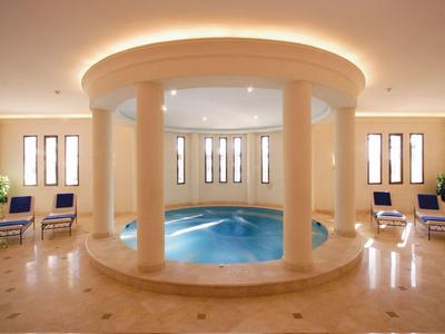 Helles Hallenbad mit rundem Pool, Säulen und Liegestühlen in einem eleganten Hotelzimmer.