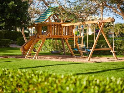 Großer Holzspielplatz mit Rutsche und Schaukeln in einem Garten mit grünem Gras.
