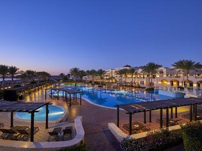 Großer Hotelpool bei Sonnenuntergang mit beleuchteten Sitzbereichen und Palmen.