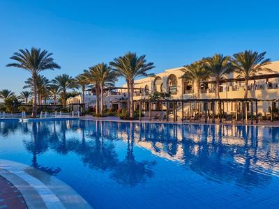 Großer Pool mit Palmen und Hotelgebäude im Hintergrund bei klarem Himmel.