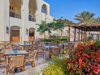 Freiluft-Terrasse eines Hotels mit Tischen, Stühlen und blühenden Pflanzen unter blauem Himmel.