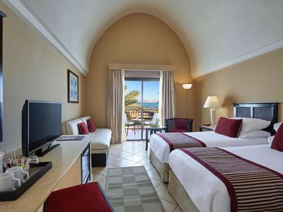 Hotelzimmer mit zwei Betten, Blick auf Terrasse und Meer, helle Wände, moderne Einrichtung.