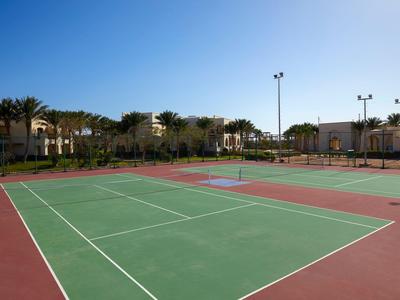 Ein leerer Tennisplatz mit rotem und grünem Belag bei klarem Himmel im Hotelbereich.
