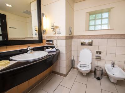 Bagno d'hotel luminoso con doccia, lavabo, toilette e bidet in tonalità neutre.