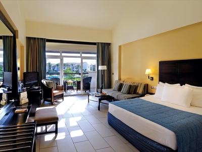 Camera d'hotel luminosa con letto grande, area salotto e balcone con vista sulla città e sul mare.