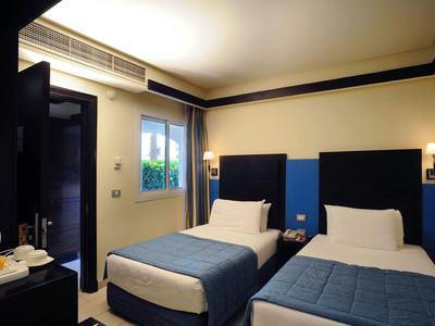 Camera d'hotel con due letti singoli, copriletti blu e finestra aperta con vista esterna.