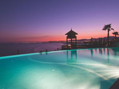 Infinity-Pool am Hotel mit Blick auf das Meer bei Sonnenuntergang und violettem Himmel.