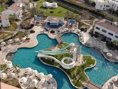 Grande piscina dell'hotel con scivolo d'acqua, lettini e edifici circostanti in un resort vacanze.