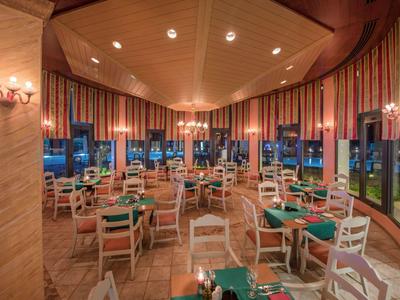 Eleganter Hotelrestaurant mit runden Tischen, grünen Tischdecken und großen Fenstern bei Dämmerung.