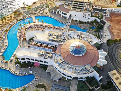 Luftaufnahme eines Hotelresorts mit Pools, Terrassen und Blick auf das Meer am Ufer.