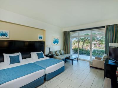 Camera d'hotel luminosa con due letti, design blu-bianco e terrazza con vista giardino.