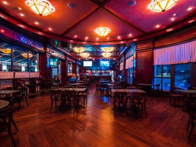 Dunkel beleuchtete Hotelbar mit Holzboden, Tischen und Stühlen unter warmen Deckenleuchten.