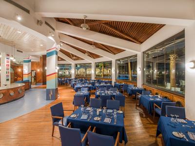 Großer Hotelrestaurantraum mit blauen Stühlen und gedeckten Tischen bei Nacht.