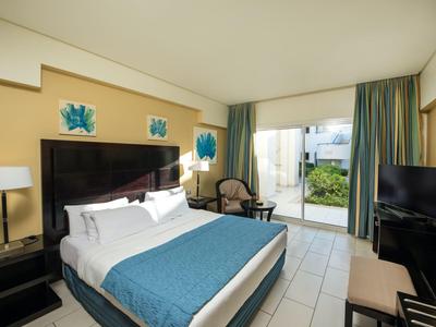 Camera d'hotel luminosa con letto matrimoniale, balcone e mobili moderni in toni neutri.