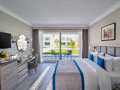 Modern eingerichtetes Hotelzimmer mit Doppelbett, Schreibtisch und Blick auf Terrasse und Pool.