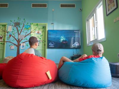 Zwei Kinder sitzen auf farbigen Sitzsäcken in einem hellen Zimmer mit grünen Wänden und einem Fernseher.