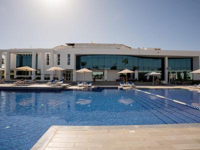Moderner Hotelkomplex mit großem Pool, weißen Sonnenschirmen und klar blauem Himmel.