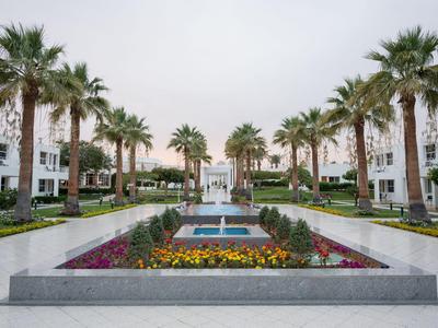 Symmetrischer Hotelgarten mit Palmen, Springbrunnen und Blumenbeeten in einer hellen Umgebung.