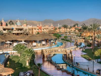 Großer Hotelkomplex mit Pools, Brücken und Palmen vor Bergkulisse unter klarem Himmel.
