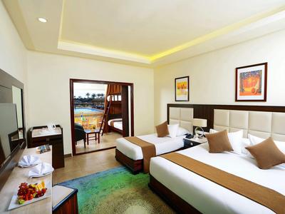 Helles Hotelzimmer mit Doppelbett, Sitzecke und Blick auf Terrasse mit Pool.