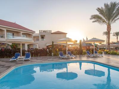 Ein Hotelpool mit Liegestühlen und Palmen bei Sonnenuntergang