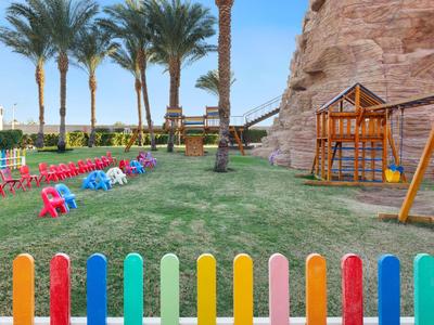 Kinderspielplatz mit bunten Stühlen, Schaukeln und Palmen neben Felsen im Hotelgarten.