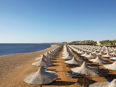 Strand mit Reihen von Sonnenschirmen aus Stroh und Sand unter klarem blauem Himmel.