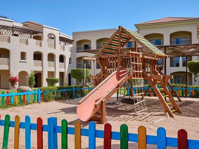 Kinderspielplatz mit Schaukel und Rutsche in einem Innenhof eines Hotels bei blauem Himmel.