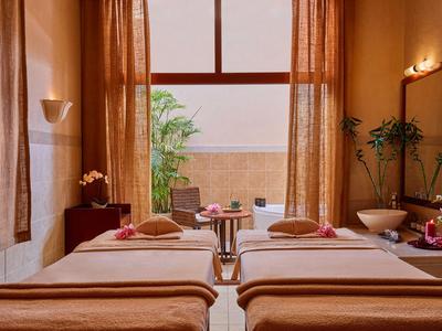 Ruhiger Spa-Raum mit zwei Massageliegen, warmen Vorhängen und entspannender Atmosphäre.