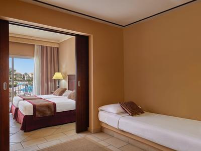 Hell eingerichtetes Hotelzimmer mit Einzelbett und angrenzendem Schlafzimmer mit Doppelbett und Blick auf das Meer.