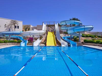 Großer Outdoor-Pool mit Wasserrutschen und klarem blauem Himmel in einer Hotelanlage.