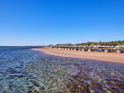 Klares Meer trifft auf einen langen Sandstrand mit Sonnenschirmen und Hotels im Hintergrund.