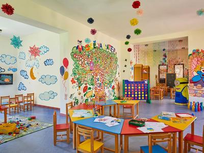 Bunter Kinderspielraum mit Tischen, Stühlen und Wandmalereien in hellem Raum eines Hotels.