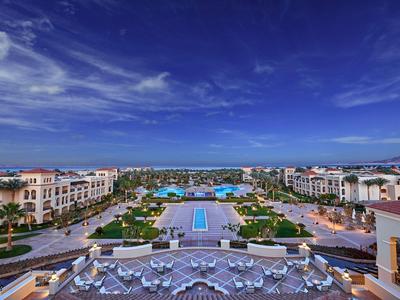 Blick auf ein luxuriöses Hotel mit großem Pool, Palmen und blauer Himmel.