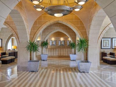 Hell beleuchtete Hotellobby mit gewölbten Steinbögen, Marmorboden und Pflanzen in Töpfen.