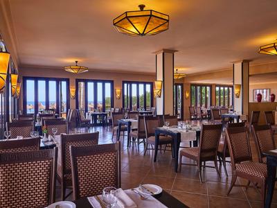 Geräumiges Restaurant mit Holztischen und Stühlen, großen Fenstern und warmem Deckenlicht.
